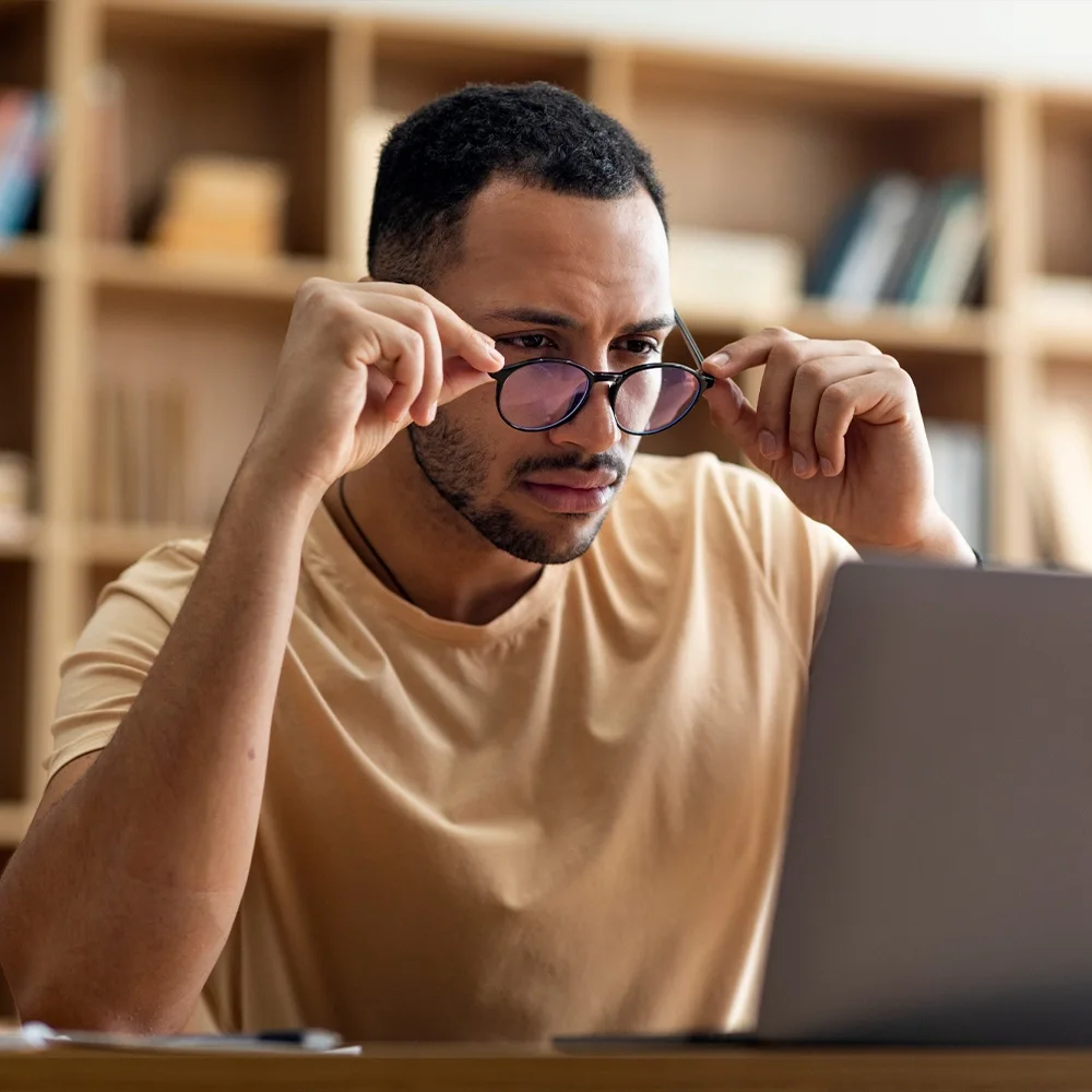 A man rubbing his eyes and struggling to focus at his laptop