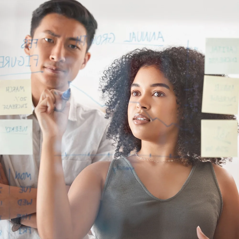 Two colleagues focused on a project at a glass board